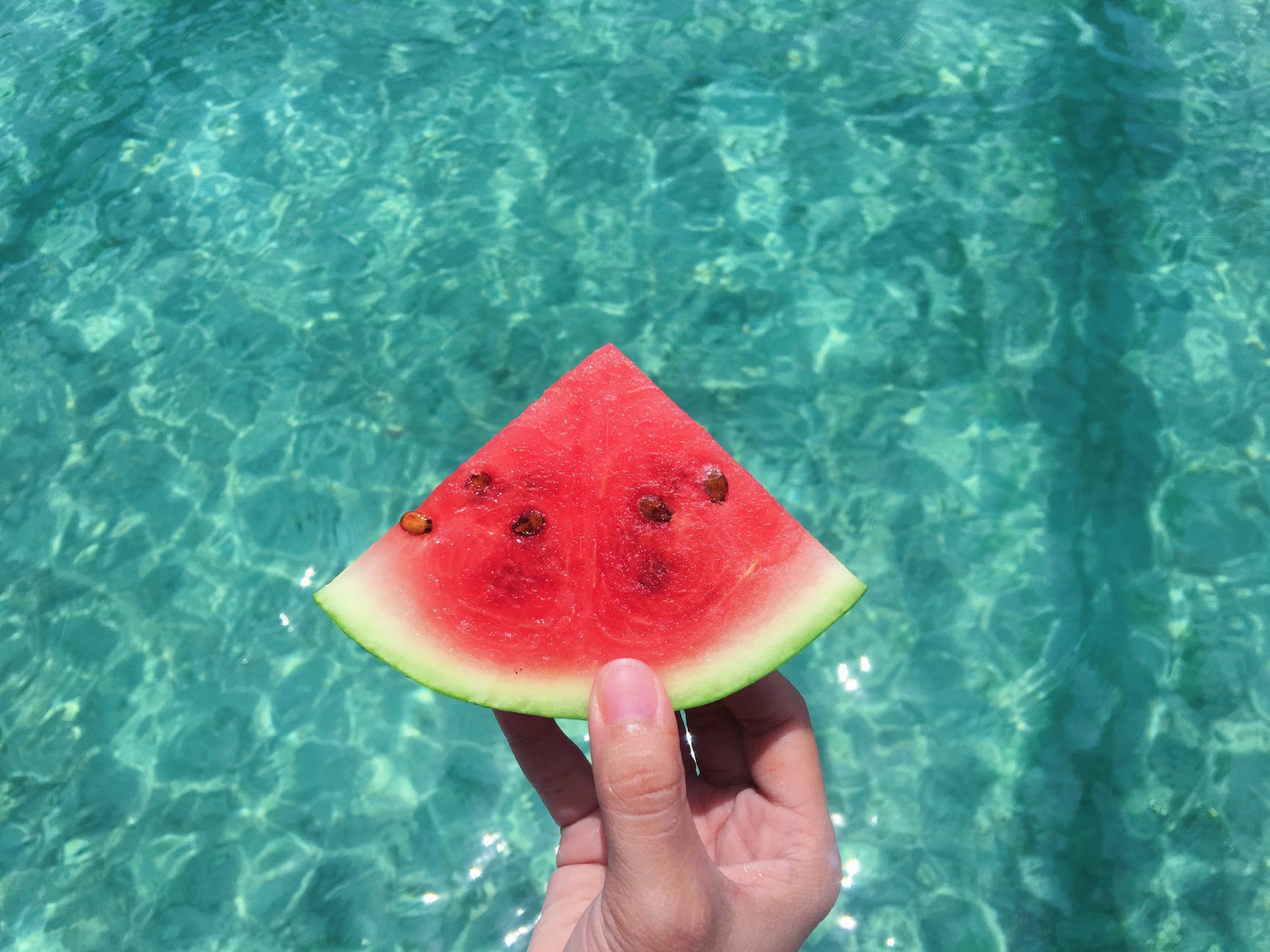 pexels-photo-2403850 - The Paris Post hand holding a slice of watermelon with blue swimming pool water in the background: Watermelon Seed benefits