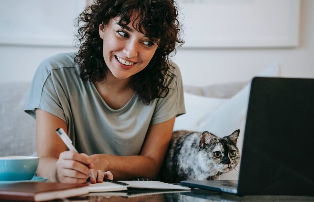 glad woman with cat writing in planner while using laptop. guest posting sites